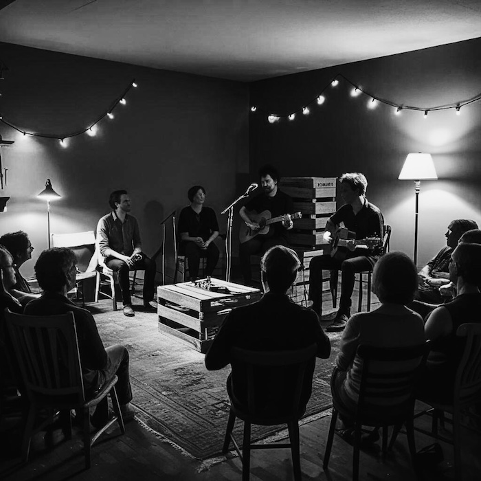Musicians performing in an intimate house setting for small audience, black & white. | Image created with Canva AI