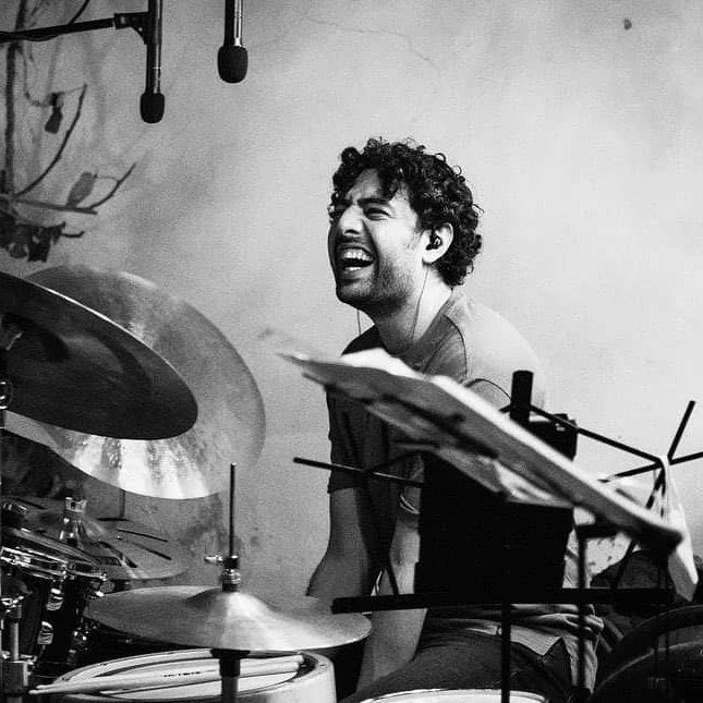 Isaac Villagomez on drum set in studio environment, laughing (black & white)